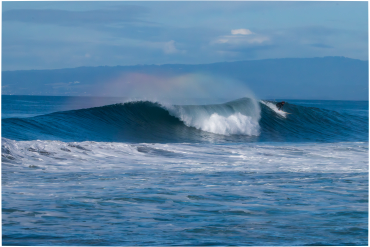 Surfer catching a wave with a rainbow in the spray.