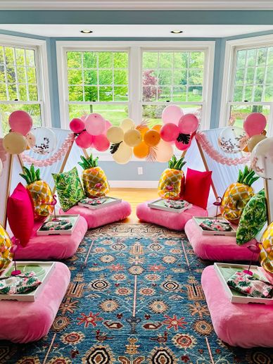 A colorful indoor party setup with pink cushions, pineapple balloons, and festive balloons.