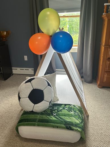 Kids' play tent with colorful balloons and soccer-themed pillows on a carpeted floor.