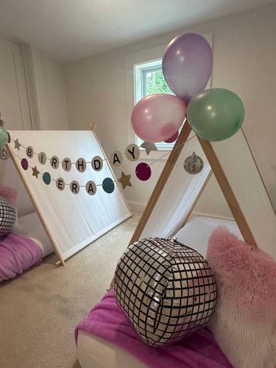 Cozy indoor birthday tent setup with balloons and disco ball decor.