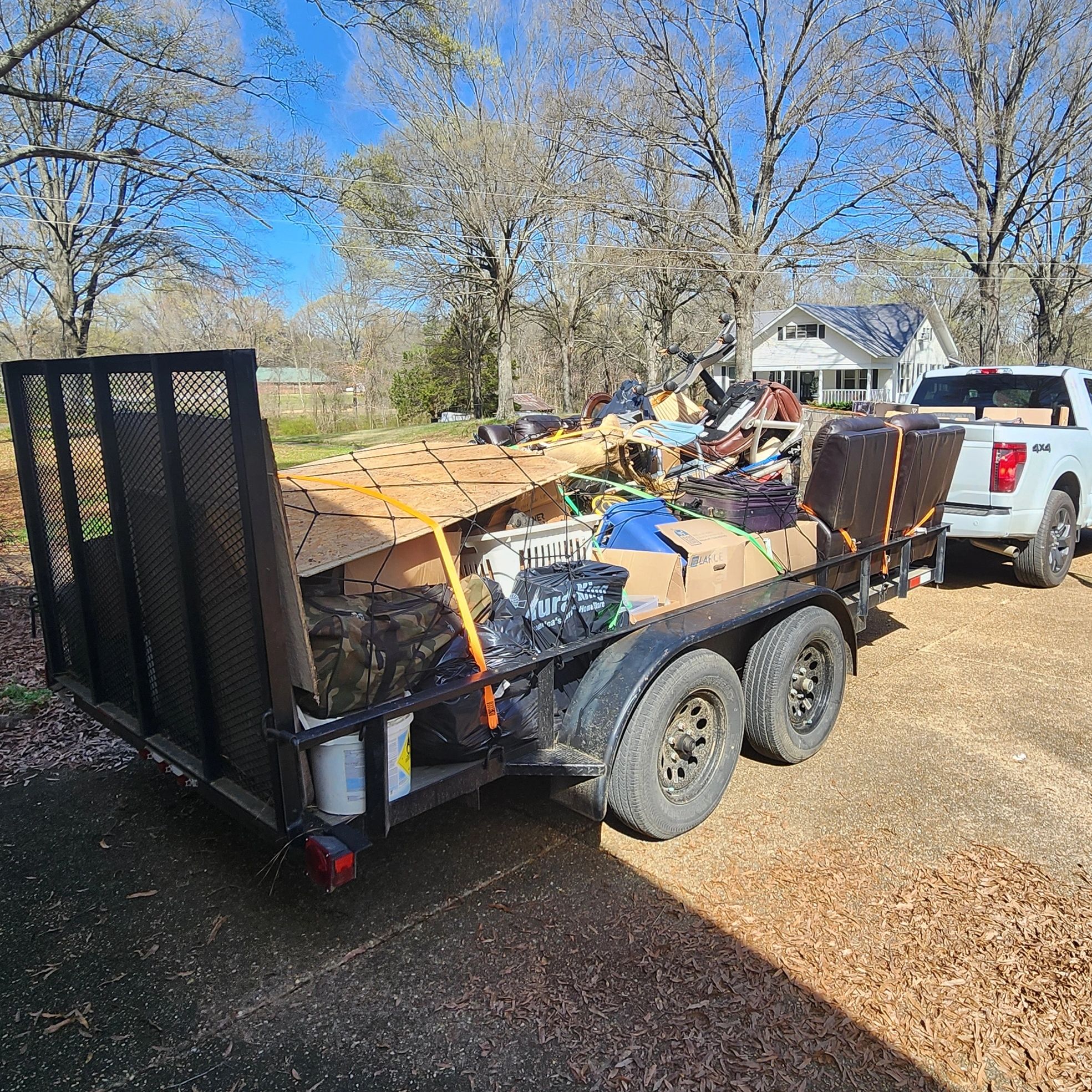 Pickup truck hauling a trailer full of assorted items under a blue sky.