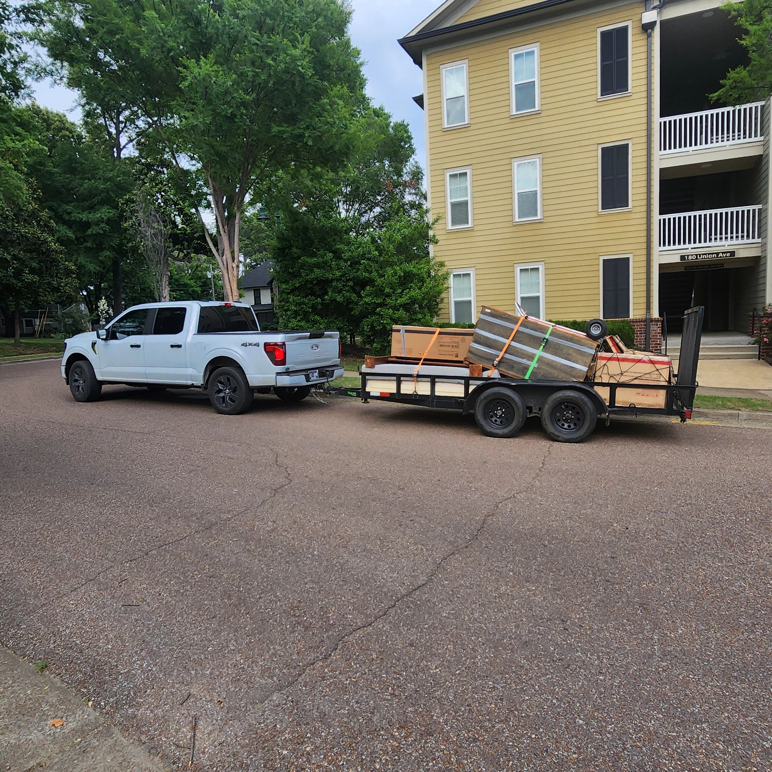 White pickup truck towing a loaded trailer near an apartment building.
