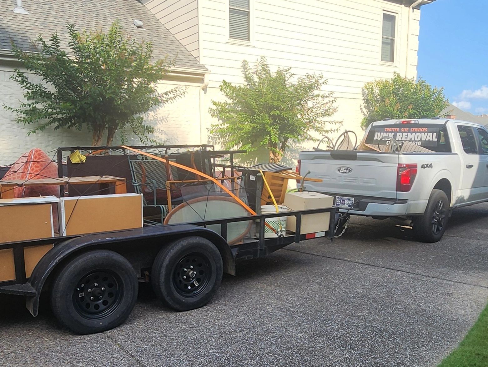 Truck with junk removal trailer loaded with furniture and household items.