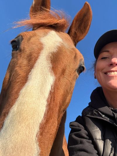 Close-up selfie of a person with a brown horse against a clear blue sky.