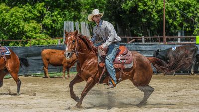 A cowboy in a white hat riding a galloping horse in an arena.