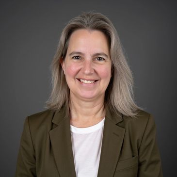 Smiling woman with gray hair wearing a brown blazer and white shirt.