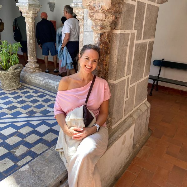 Woman in a pink top sitting and smiling by a stone pillar in a courtyard.