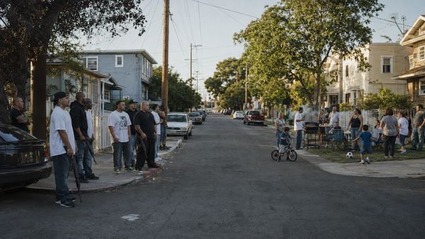 Neighborhood gathering with people standing and kids playing outside.