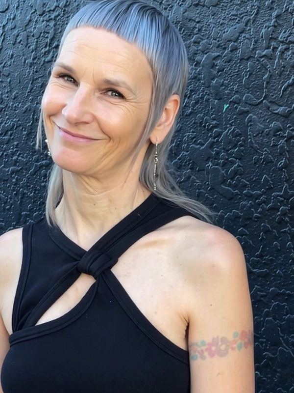 Smiling woman with short blue hair and floral tattoo on arm.