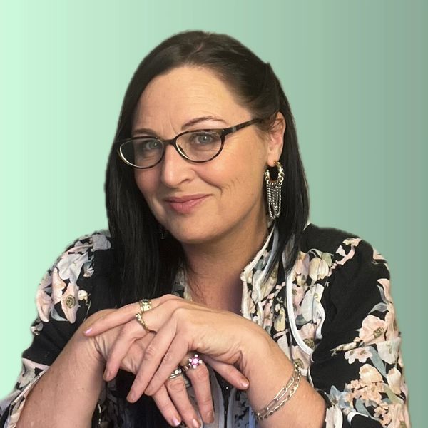 Smiling woman with glasses and floral jacket posing against green gradient background.