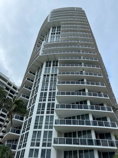 Modern high-rise building with multiple balconies and large windows under a cloudy sky.