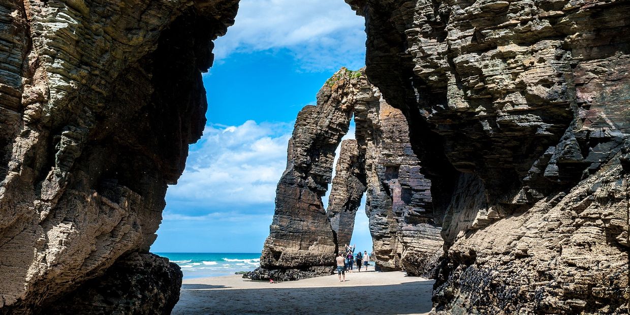 Natural rock formations on a beach with people walking.