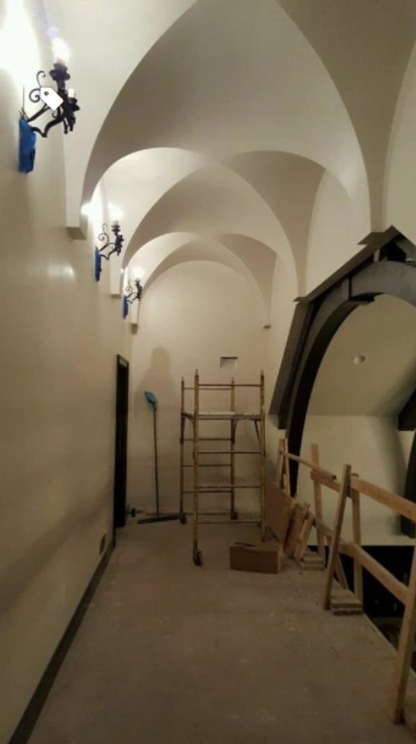 Arched hallway with scaffolding and wall lights.