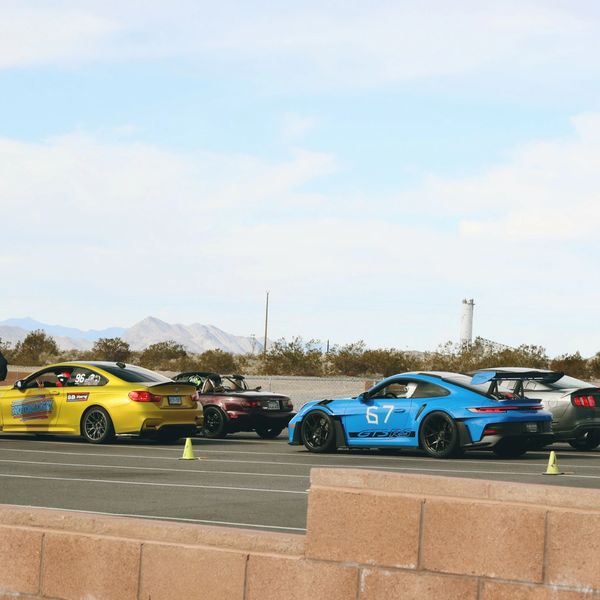 Four sports cars lined up on a race track with mountains in the background.