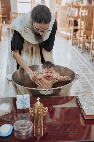 A priest baptizes a crying baby in a church baptismal font.