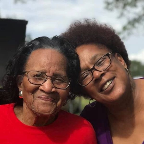 Two smiling women wearing glasses, sharing a close moment outdoors.