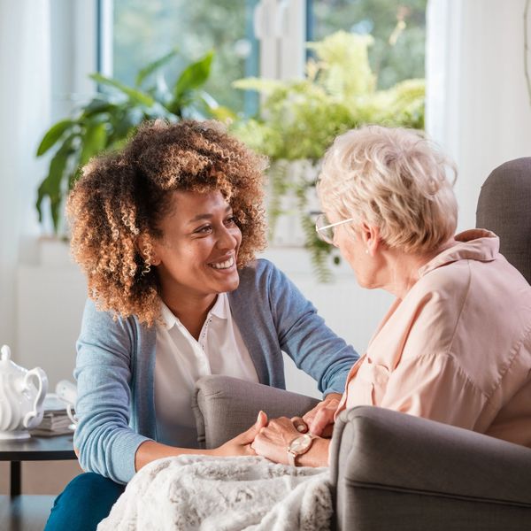 A young woman warmly holding hands with an elderly woman in a cozy living room.