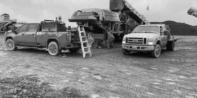 two service trucks parked in front of large crusher conveyhor belt