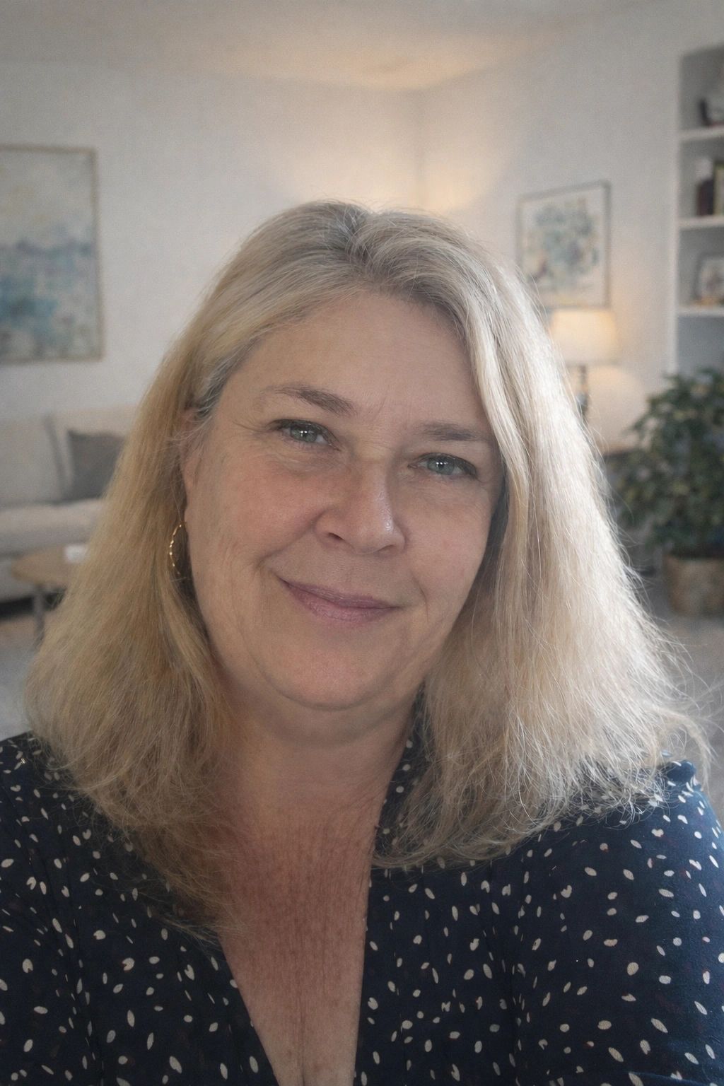 Smiling middle-aged woman with blonde hair in a cozy living room.