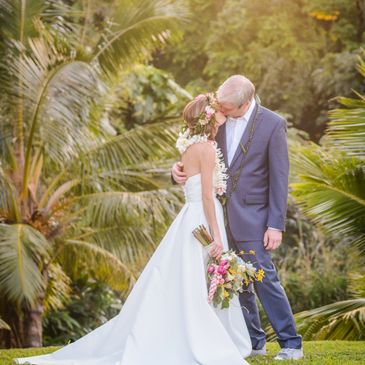 Hawaii Bride and groom Kauai Island Weddings Pacific Wedding bride with haku head lei and tropical wedding bouquet kissing under palm trees garden Kauai wedding venues