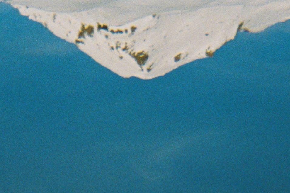 Snow-covered mountain peak reflected in calm blue water.