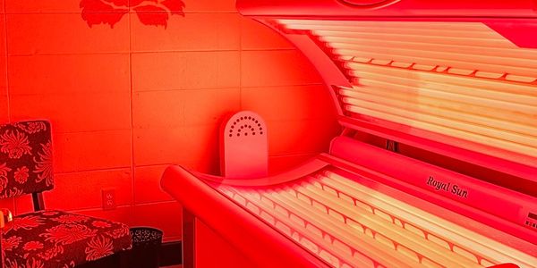 Interior of a red-lit tanning salon with a tanning bed and chair.