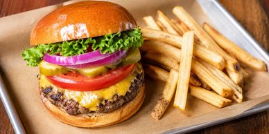 Cheeseburger with lettuce, tomato, onion, pickles, and fries on a tray.