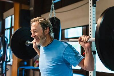 Smiling man lifting a barbell in a gym.
