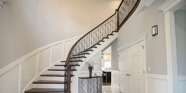 Elegant curved staircase with wrought iron railing in a bright, modern hallway.