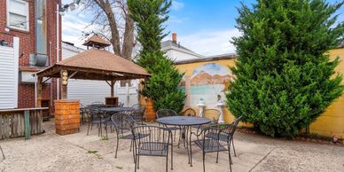Outdoor patio with metal tables and chairs under a gazebo and open sky.