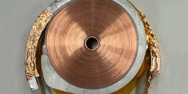 Close-up of a copper coil wrapped around a metallic core with gold foil on the sides.