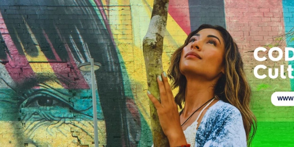 A woman looks up beside colorful mural at CODIGGO Culture Lab.