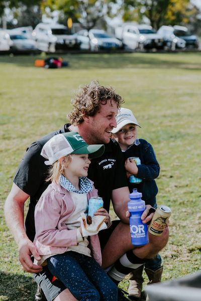 Man with two children enjoying drinks outdoors, smiling and relaxed.
