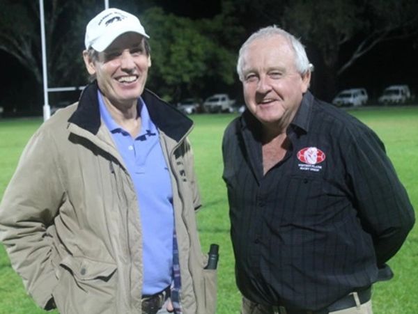Two older men smiling outdoors on a grassy field at night.