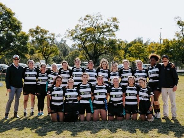 Women's rugby team posing outdoors in black and white striped uniforms.