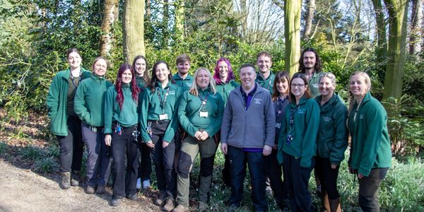 Group of people in green jackets posing outdoors in a wooded area.