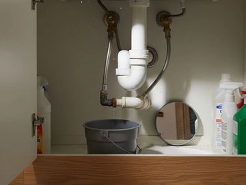 Leaking pipe under sink with bucket catching drips.