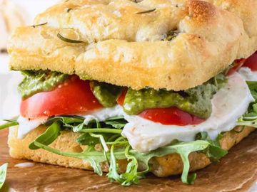 Close-up of a fresh sandwich with tomato, mozzarella, and greens on focaccia bread.