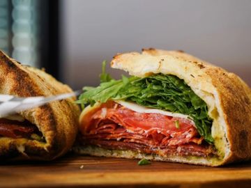 A close-up of a sandwich with layers of meat, tomato, and leafy greens.