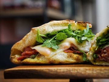 Close-up of a sandwich filled with greens, melted cheese, and bacon.