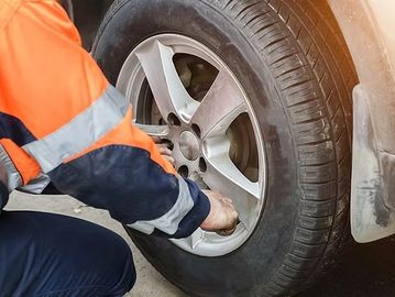 Person in safety gear tightening lug nuts on a car tire.