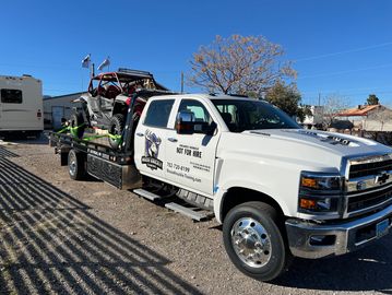 White tow truck transporting an off-road vehicle on a clear day.