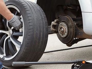 Person changing a car tire using a jack and gloves.