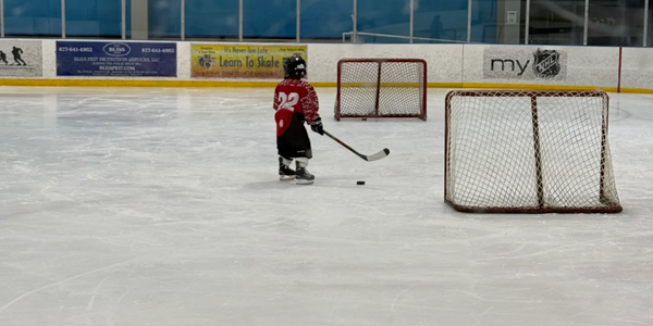 Young hockey player practicing on ice rink with two goals.