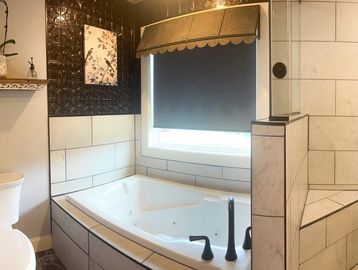 Modern bathroom with large bathtub and dark window shade.