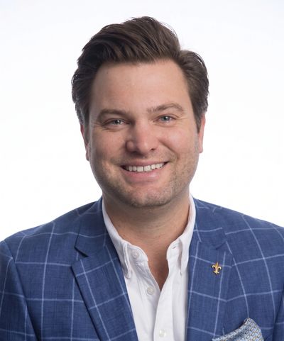 Smiling man in a blue checked blazer and white shirt.