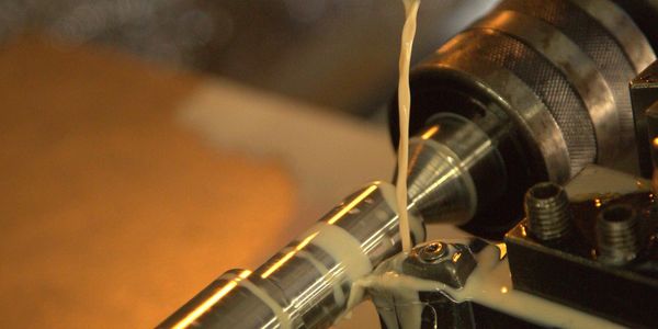 Metalworking lathe machine with coolant fluid flowing on a metal rod.