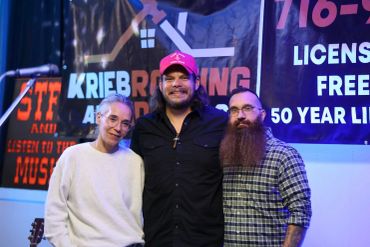 Three smiling people posing in front of a music event banner.