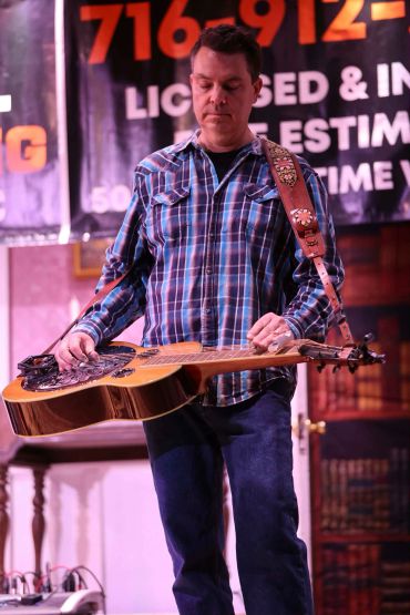 Man playing resonator guitar on stage with a focused expression.