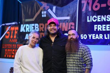 Three people posing happily in front of a Krieb Roofing banner.